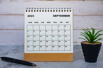 September 2023 desk calendar with table plant and pen.