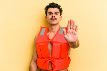 Young caucasian man wearing life jacket isolated on yellow background standing with outstretched...