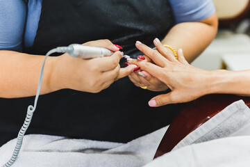 Manicurist is applying electric nail file drill to manicure on female fingers.
