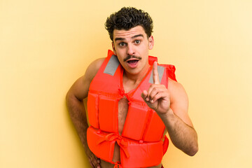 Young caucasian man wearing life jacket isolated on yellow background having an idea, inspiration...