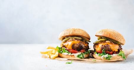Two craft cheeseburgers and fries on parchment paper over grey concrete background. Copy space. Web banner burgers - 519164135