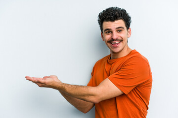 Young caucasian man isolated on blue background holding a copy space on a palm.