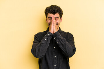 Fototapeta premium Young caucasian man isolated on yellow background holding hands in pray near mouth, feels confident.