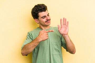 Young caucasian man isolated on yellow background smiling cheerful showing number five with fingers.