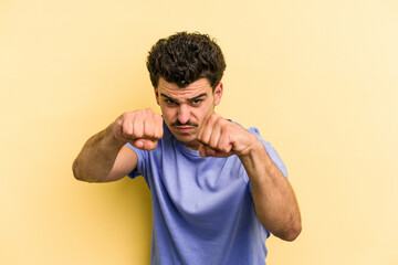 Young caucasian man isolated on yellow background throwing a punch, anger, fighting due to an argument, boxing.