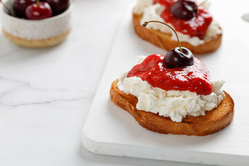 Appetizer with ricotta cheese, cream cheese, jam and cherry on white board and marble table. Toast, snack, bruschetta.