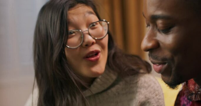 An Asian-looking girl with glasses and young African-looking guy unpack Christmas presents. The girl is infinitely happy and pleasantly surprised to receive the long-awaited gift.