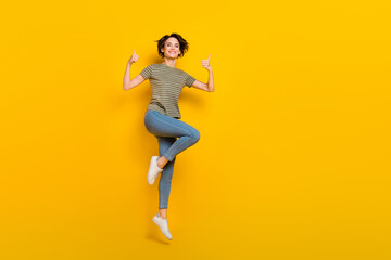 Fototapeta na wymiar Full length photo of adorable confident girl dressed green t-shirt jumping thumbs up empty space isolated yellow color background