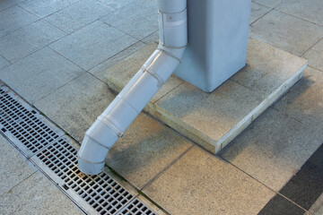 Metal drain pipe with a shoe for a drain pipe at the end. Fastened to a metal concrete support. Leading to a black metal square gutter grate on grant slabs. - obrazy, fototapety, plakaty