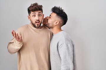 Young homosexual couple standing over white background hand on mouth telling secret rumor,...