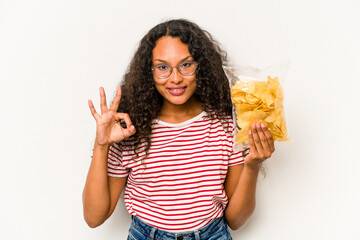 Young hispanic woman holding crips isolated on white background cheerful and confident showing ok gesture.