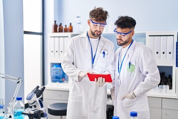 Young couple wearing scientist uniform using touchpad at laboratory