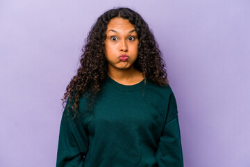 Young hispanic woman isolated on purple background blows cheeks, has tired expression. Facial expression concept.