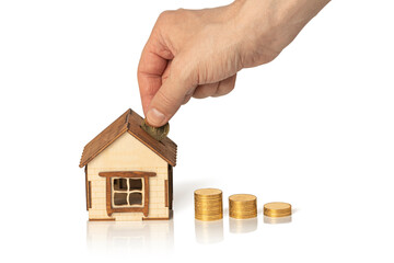 Small wooden house and coins stacks isolated on white background. Man's hand puts a coin in the house. Mortgage and real estate investment concept. Copy space.