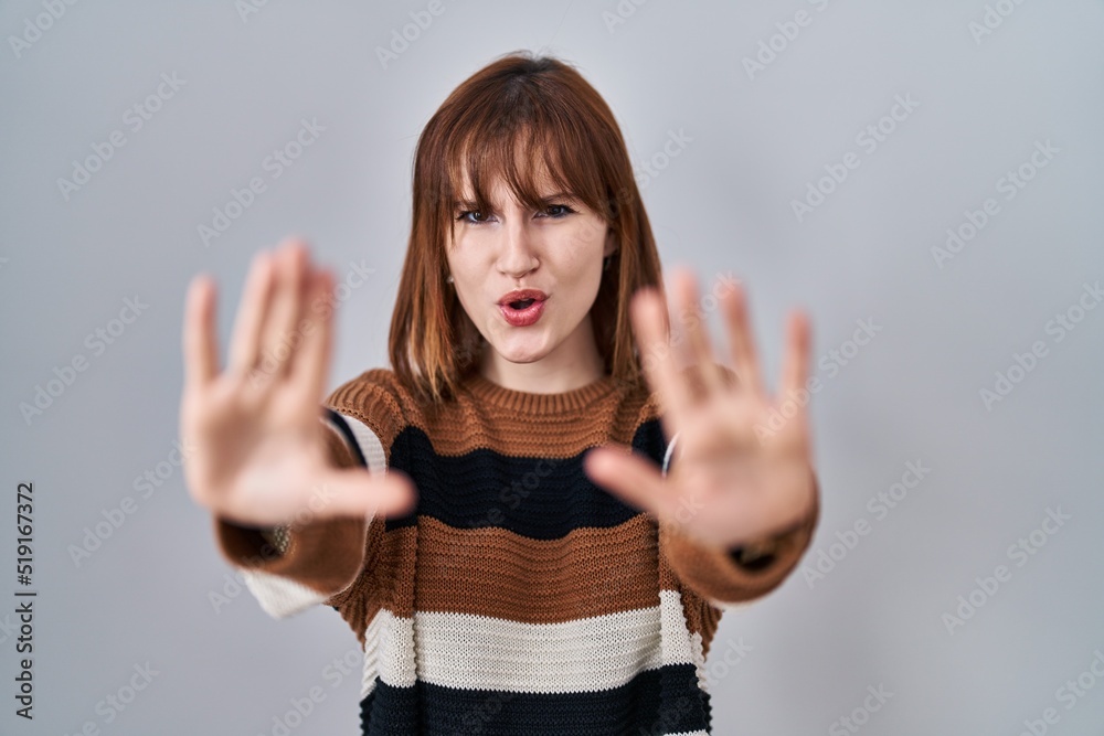 Poster Young beautiful woman wearing striped sweater over isolated background doing stop gesture with hands palms, angry and frustration expression