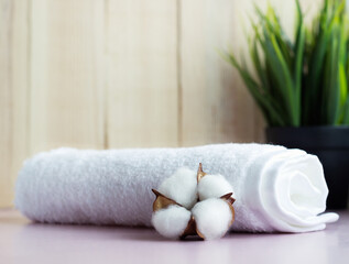 Rolled white towel with cotton flower on the pink table with wooden background