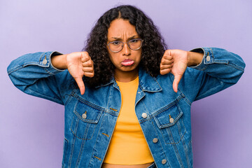Young hispanic woman isolated on purple background showing a dislike gesture, thumbs down....