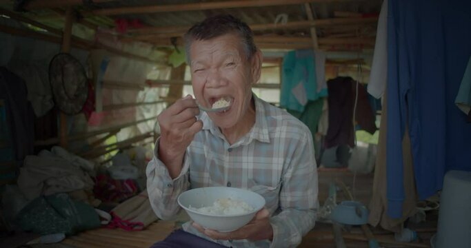 Slow motion of an Asian man who is  a poor elderly native and works as a wage earner in a farm, live in a poor house, eating rice and smiling happily.
