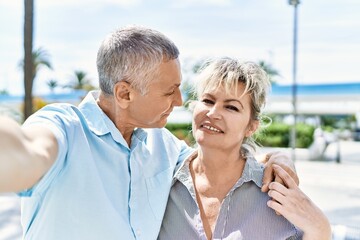 Middle age caucasian couple of husband and wife together on a sunny day outdoors. Smiling happy in love hugging taking a selfie picture