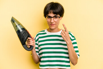 Young caucasian woman holding a hand vacuum cleaner isolated on yellow background pointing with finger at you as if inviting come closer. © Asier