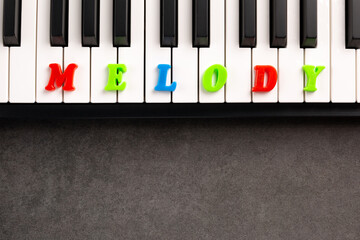 The word melody is composed of multicolored letters on the piano keys. Copy space.	