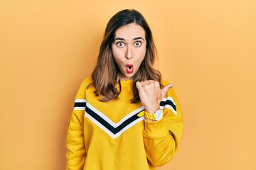 Young hispanic girl wearing casual clothes surprised pointing with hand finger to the side, open mouth amazed expression.