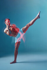 Muscular athletic male fighter kicking, raised leg up on blue studio backdrop. Motion blur. Sport...