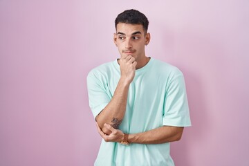 Handsome hispanic man standing over pink background looking stressed and nervous with hands on mouth biting nails. anxiety problem.