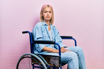 Beautiful blonde woman sitting on wheelchair relaxed with serious expression on face. simple and...