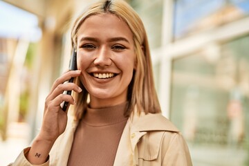 Young blonde girl smiling happy talking on the smartphone at the city.