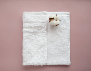 Folded white cotton towel with cotton flower on the light background.