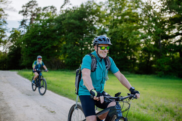 Active senior couple riding electric bicycles on trail at summer park, healthy lifestyle concept.