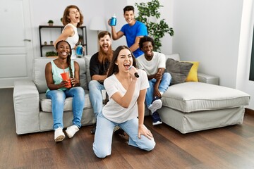 Group of young friends having party singing song using microphone at home.