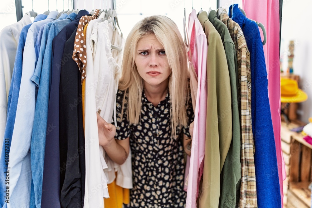 Canvas Prints young blonde woman searching clothes on clothing rack skeptic and nervous, frowning upset because of