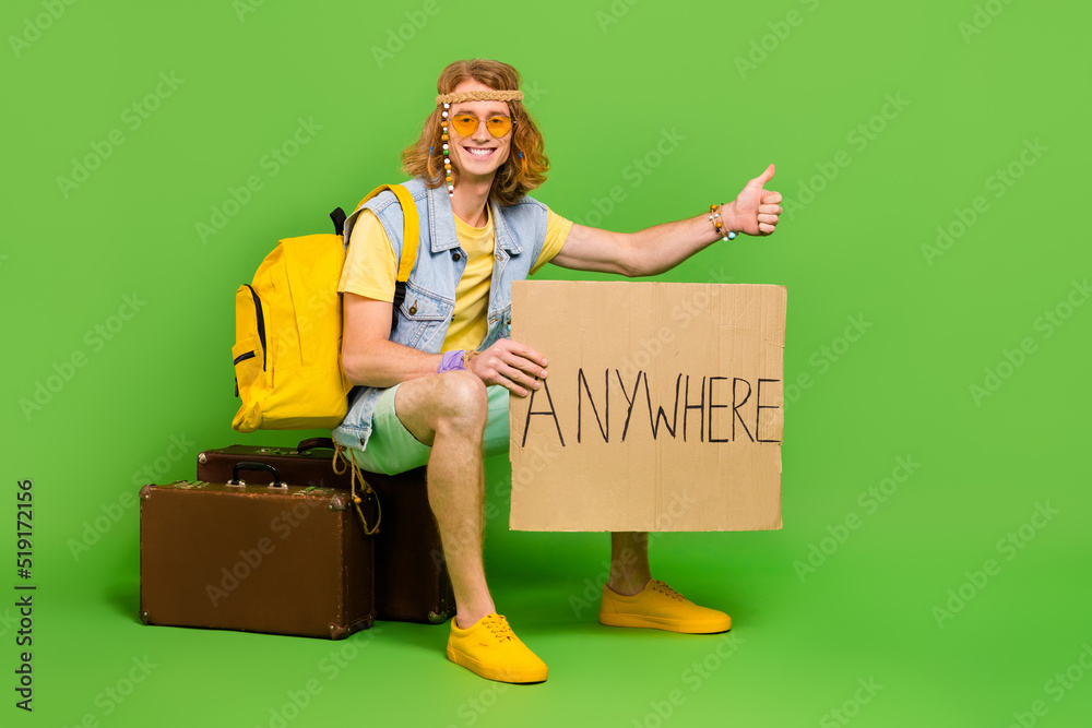 Poster full size photo of positive hippy person sitting suitcase thumb up hitchhike isolated on green color