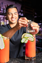Smiling waiter adds pepper to a red cocktail