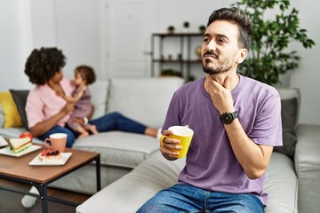 Hispanic father of interracial family drinking a cup coffee touching painful neck, sore throat for flu, clod and infection