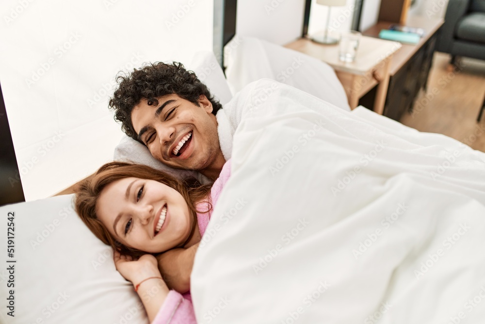 Poster young couple smiling happy and hugging lying on the bed at bedroom.