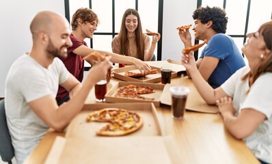 Group of young friends smiling happy eating italian pizza sitting on the table at home.
