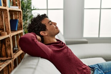 Young hispanic man relaxing with hands on head sitting on the sofa at home.