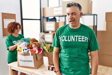 Middle age man wearing volunteer t shirt at donations stand winking looking at the camera with sexy expression, cheerful and happy face.