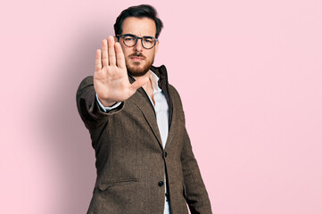 Young hispanic man wearing business jacket and glasses doing stop sing with palm of the hand. warning expression with negative and serious gesture on the face.