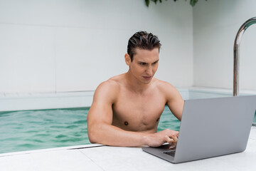 sportive man with wet hair using laptop near pool.