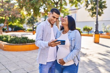 Young latin couple expecting baby using smartphone at park