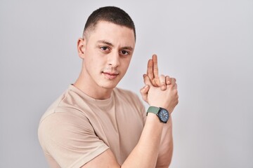 Young man standing over isolated background holding symbolic gun with hand gesture, playing killing shooting weapons, angry face