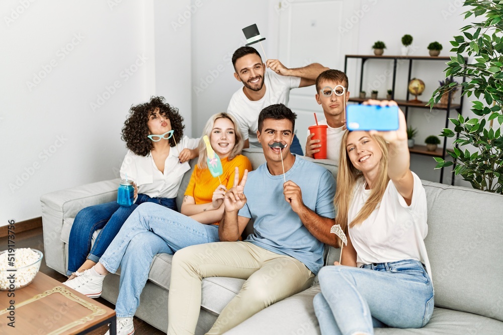 Poster group of young friends using funny costume accessories making selfie by the smartphone at home.