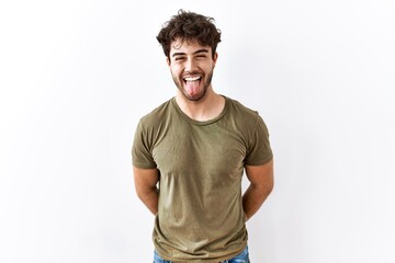 Hispanic man standing over isolated white background sticking tongue out happy with funny expression. emotion concept.