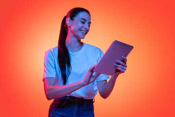 Portrait of young emotional girl, student in white t-shirt isolated on orange color background in...