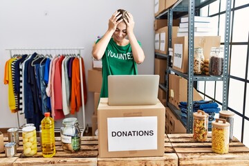 Young blonde woman wearing volunteer t shirt at donations stand suffering from headache desperate...