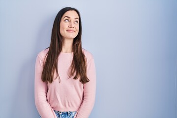 Obraz premium Young brunette woman standing over blue background smiling looking to the side and staring away thinking.